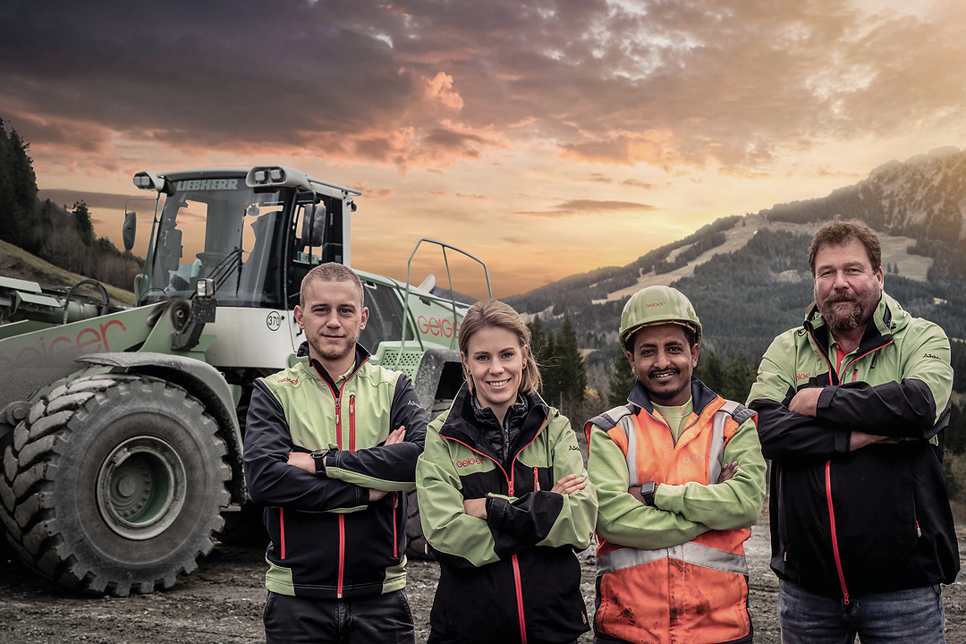 Vier Personen in Geiger Arbeitskleidung vor einem Geiger Bagger.
